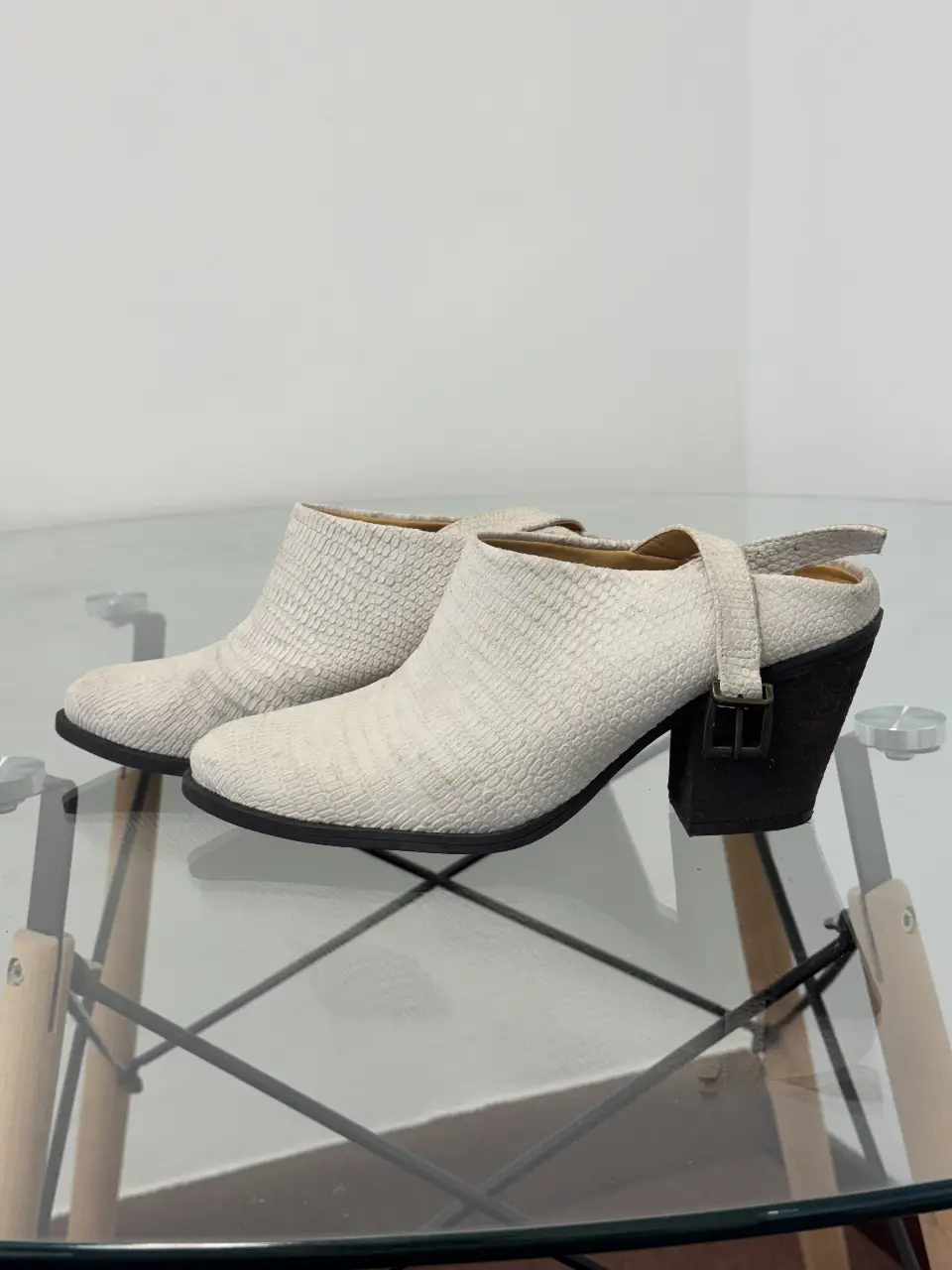 Botines blancos con taco negro y hebilla en el tobillo. Diseño con textura símil reptil, ideales para un look moderno y sofisticado.