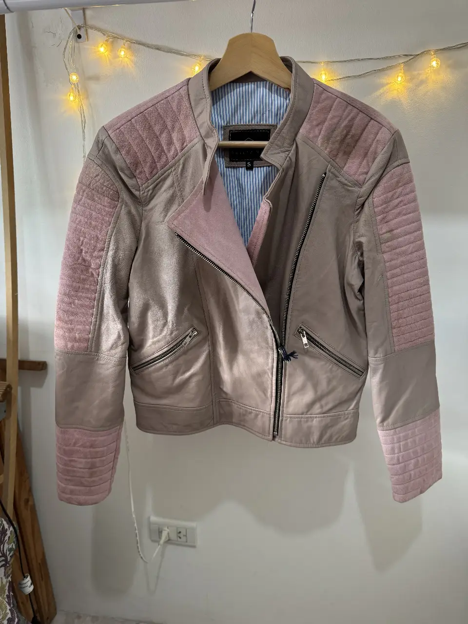 Campera biker de cuero sintético en tonos rosa y gris. Detalles acolchados en hombros y mangas, cierre asimétrico y bolsillos con cierres. Ideal para un look moderno y canchero.