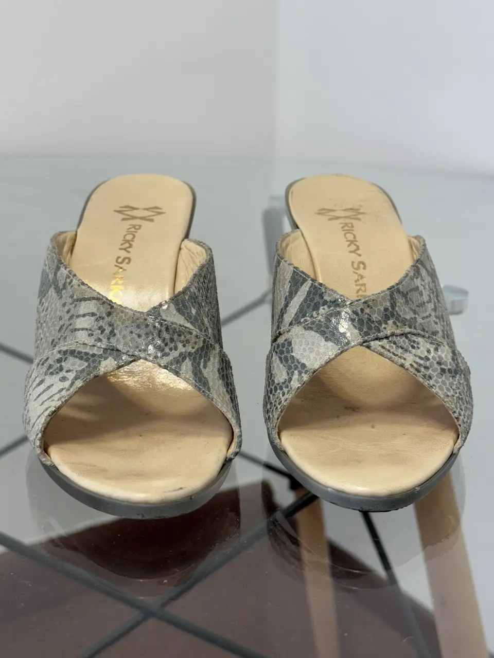 Sandalias Ricky Sarkany con diseño de serpiente en tonos grises. Tacón ancho y detalle cruzado en la parte delantera. Ideales para un look elegante y sofisticado.