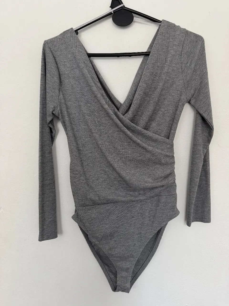 Body de manga larga gris con diseño envolvente y fruncido en la cintura. Ideal para un look moderno y versátil.
