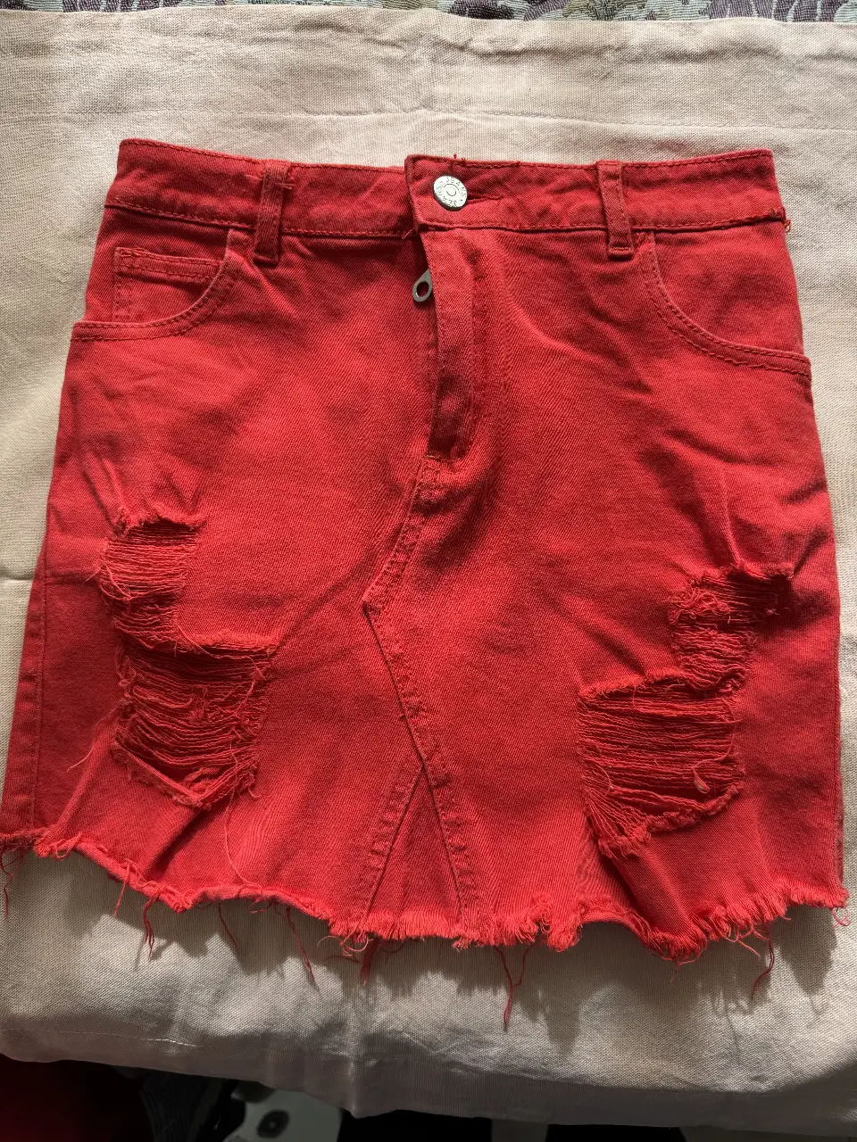 pollera de jean rojo con roturas y detalles desflecados. Tiro medio, ideal para un look casual y moderno.
