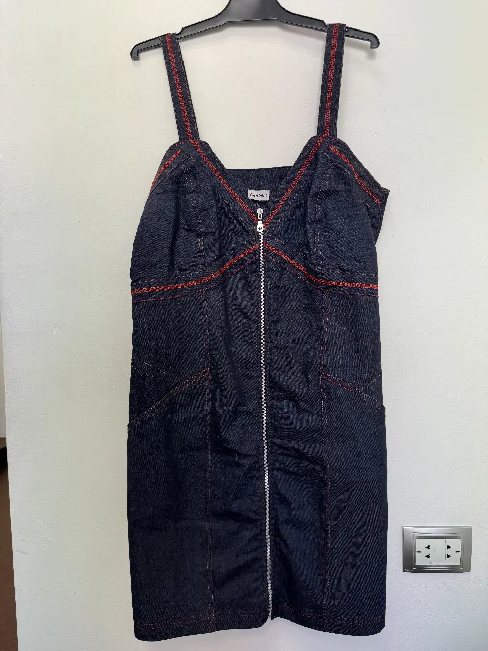 Vestido mini de jean azul oscuro con detalles en rojo. Tiene cierre frontal y tiras rojas. Ideal para un look casual y moderno.