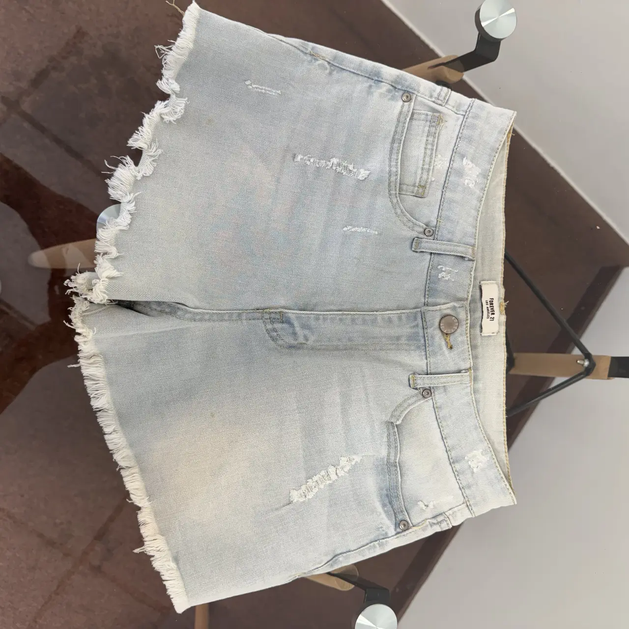 Short de jean celeste claro con detalles de roturas y flecos en el borde. Ideal para un look casual y fresco.