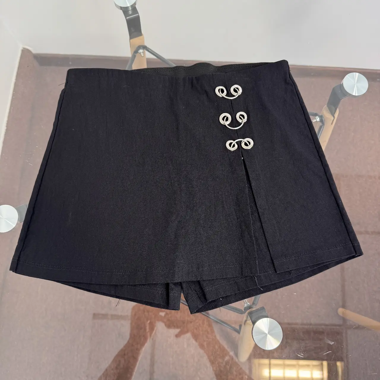 Short negro con detalle de botones plateados. Diseño con corte en la parte delantera, ideal para un look moderno y versátil.