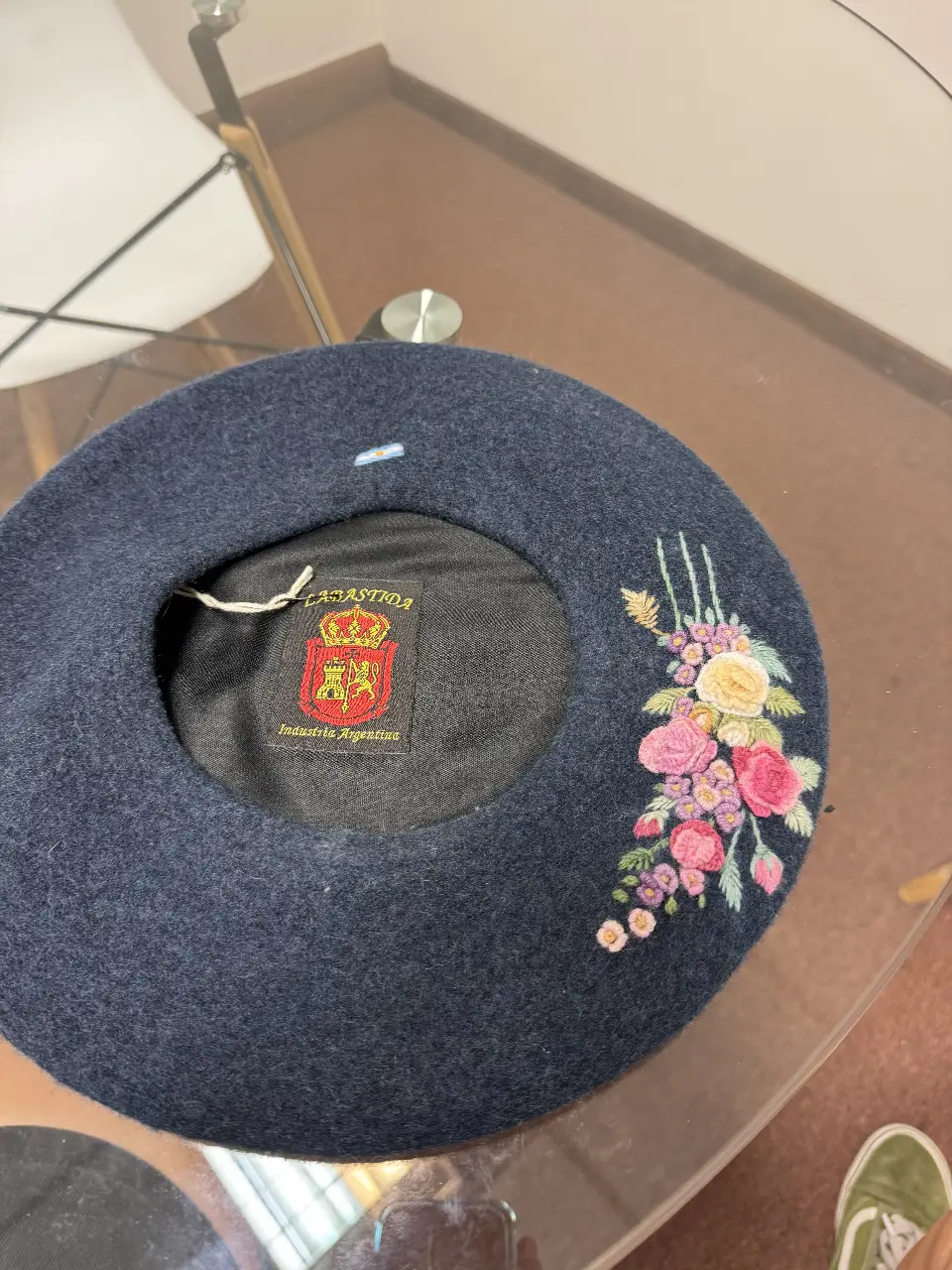 Boina azul marino de fieltro con bordado floral en tonos rosas, amarillos y verdes. Detalles de la marca "La Bastida" y "Industria Argentina". Ideal para un look artesanal y romántico.