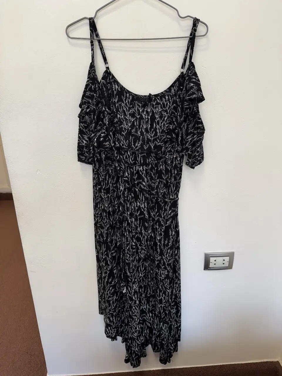 Vestido midi negro con estampado floral blanco. Diseño con hombros descubiertos y volados. Ideal para un look fresco y femenino.