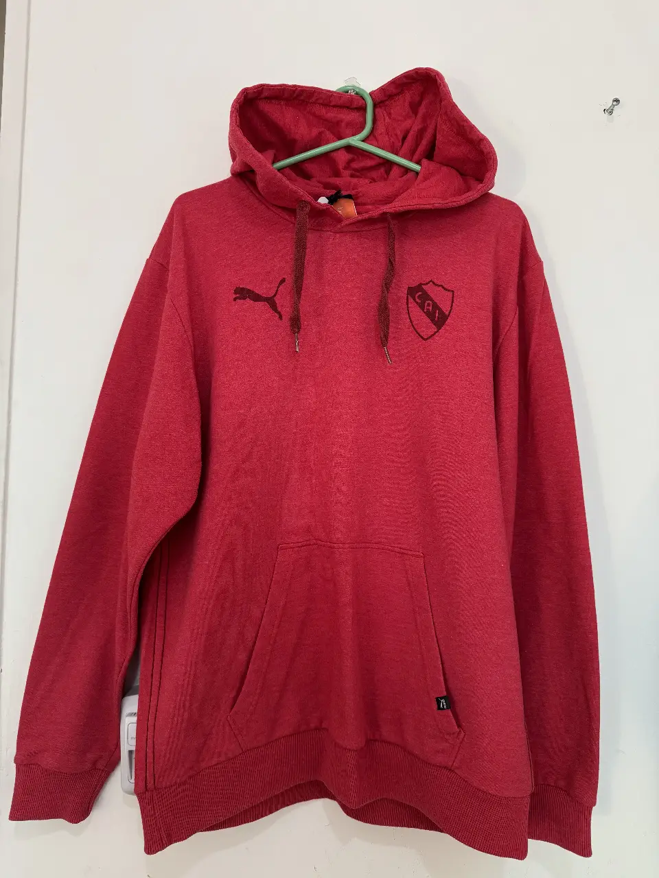 Buzo canguro rojo de hombre, con capucha y bolsillo delantero. Con logo de Puma y escudo del club CAI.
