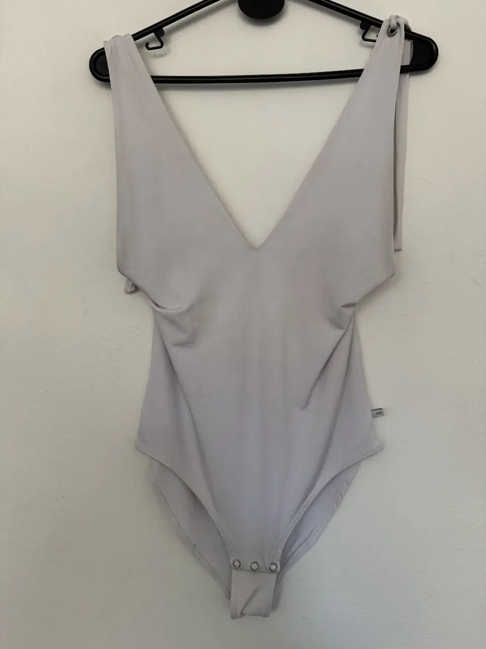 Body de mujer en color gris claro, con escote en V pronunciado y tiras para atar en los hombros. Ideal para un look elegante y moderno.