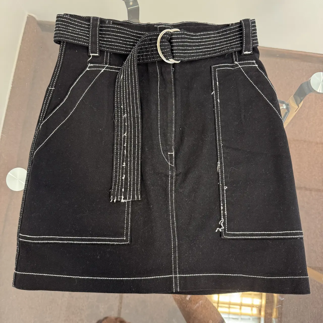 Pollera negra de jean con detalles de costura blanca y cinturón a juego. Posee bolsillos delanteros y traseros, ideal para un look casual y moderno.