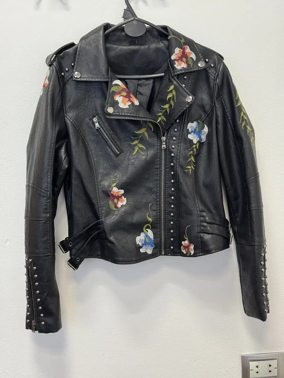 Campera biker de cuero sintético negra con bordados florales. Detalles de tachas en hombros y mangas, cierre asimétrico y detalles de hebillas. Talle M.