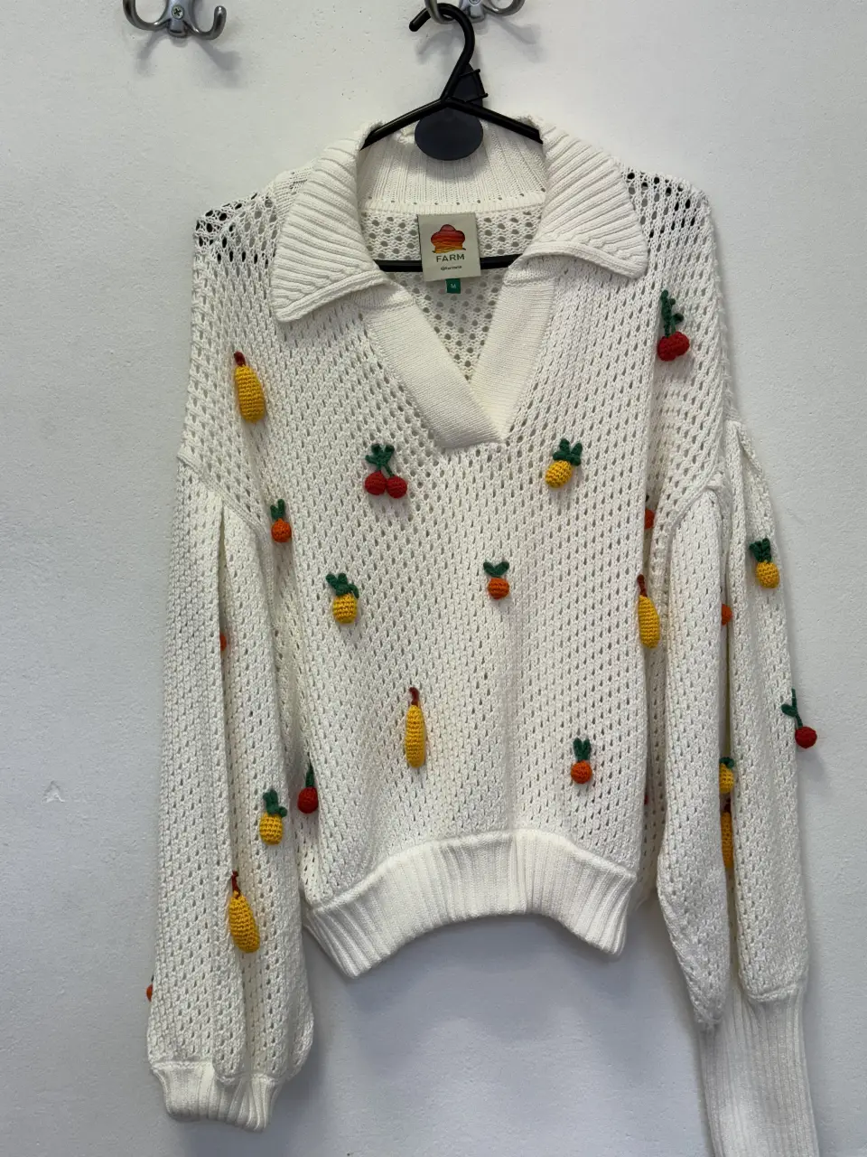 Sweater blanco de punto calado con detalles de frutas tejidas en relieve. Cuello en V y mangas amplias. Ideal para un look fresco y original.