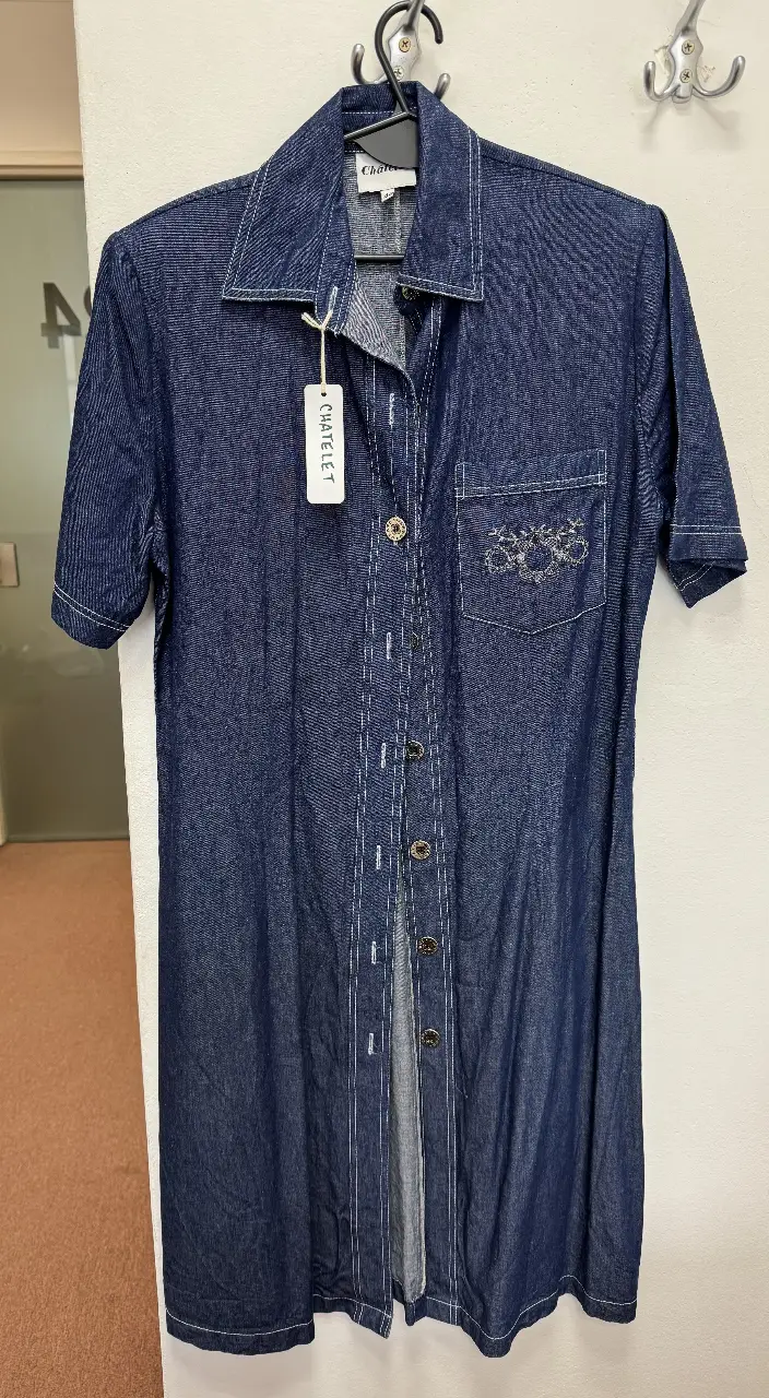 Vestido midi de jean azul con botones y bolsillo bordado. Ideal para un look casual y cómodo.