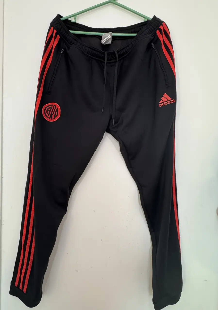 Pantalón deportivo Adidas negro con detalles rojos y el escudo de River Plate. Ideal para entrenar o usar en el día a día. Talles disponibles.