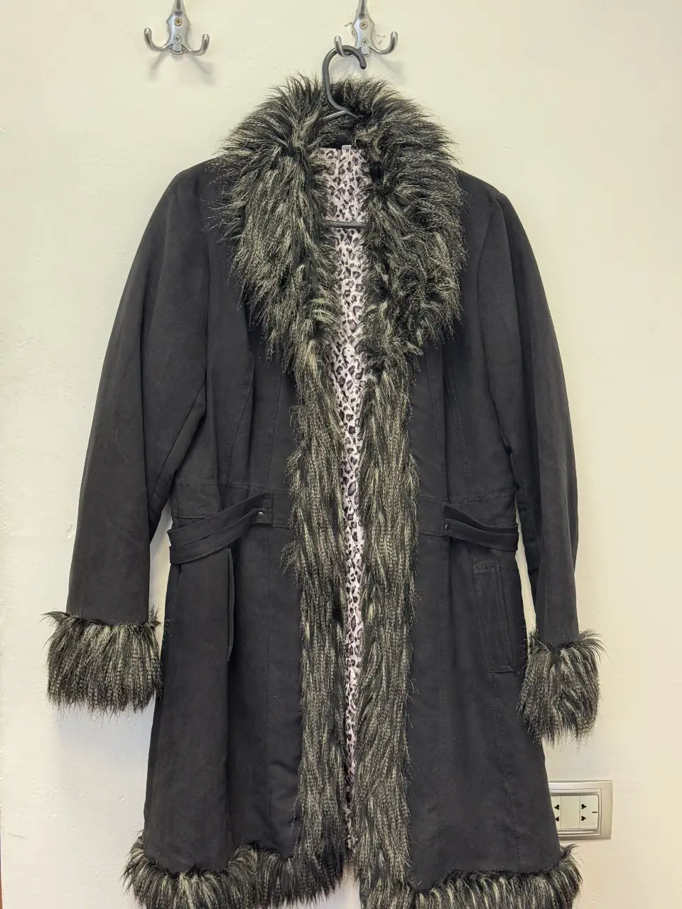 Tapado largo negro con detalles de piel sintética en cuello, borde y puños. Interior con estampado animal print. Ideal para un look elegante y abrigado en invierno.