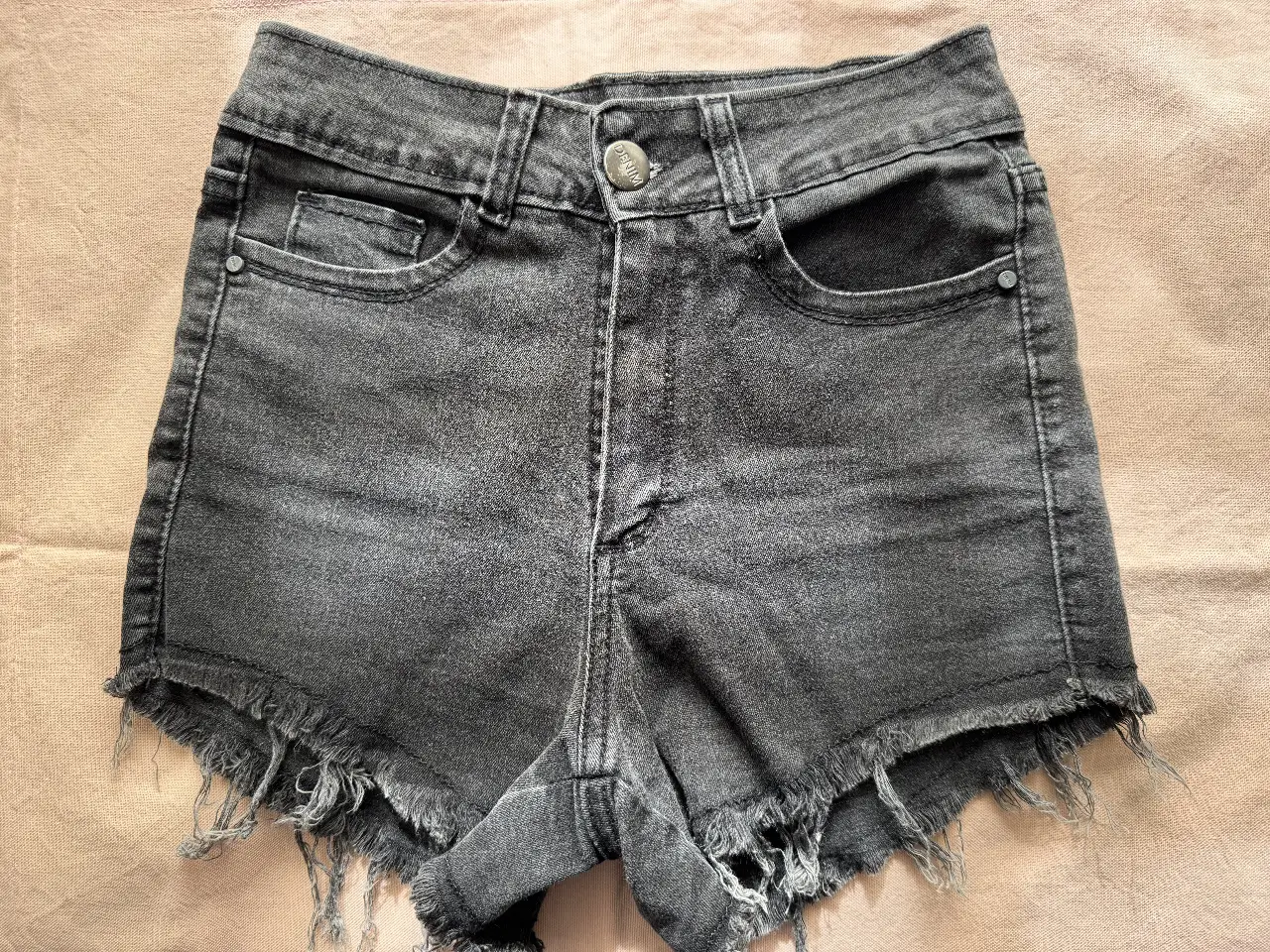 Short de jean negro con flecos en el borde. Tiro medio y calce ajustado. Ideal para un look casual y moderno.