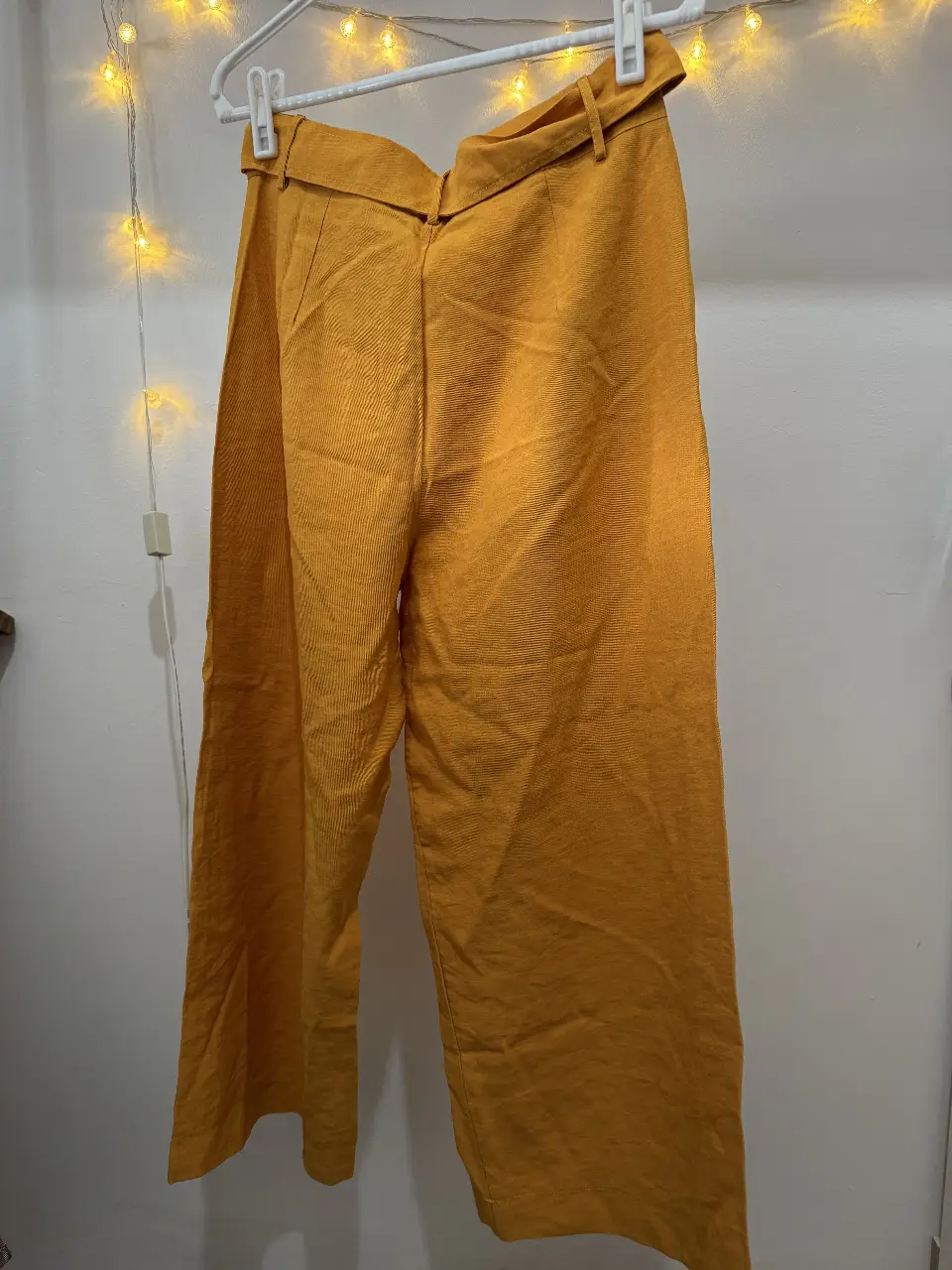 Pantalón sastrero de corderoy color mostaza con cinturón. Tiene bolsillos delanteros y cierre con botón y cremallera. Ideal para un look casual o de trabajo.