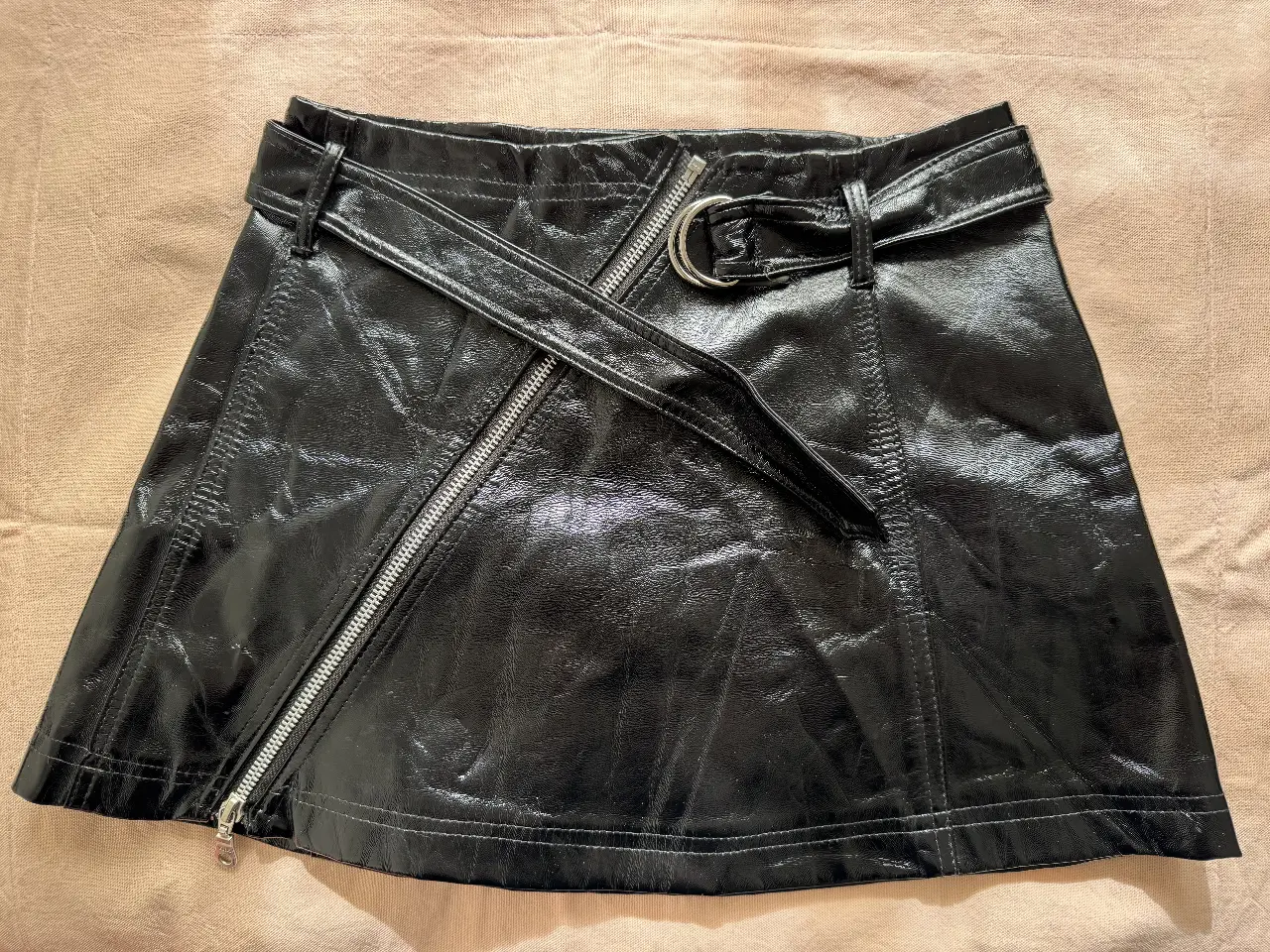 Minifalda negra de cuero sintético con cierre asimétrico y cinturón. Ideal para un look moderno y audaz.