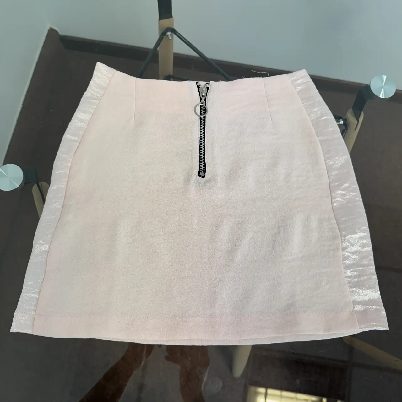 Pollera rosa de tela con detalles satinados en los laterales. Tiene cierre en el frente y es ideal para un look elegante y moderno.
