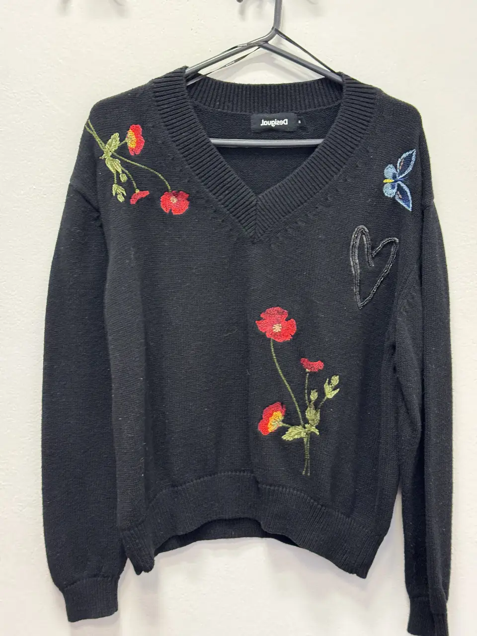 Sweater negro de mujer con cuello en V y bordados florales. Diseño Desigual con detalles de flores rojas y amarillas, un corazón y una mariposa. Ideal para un look casual y con estilo.