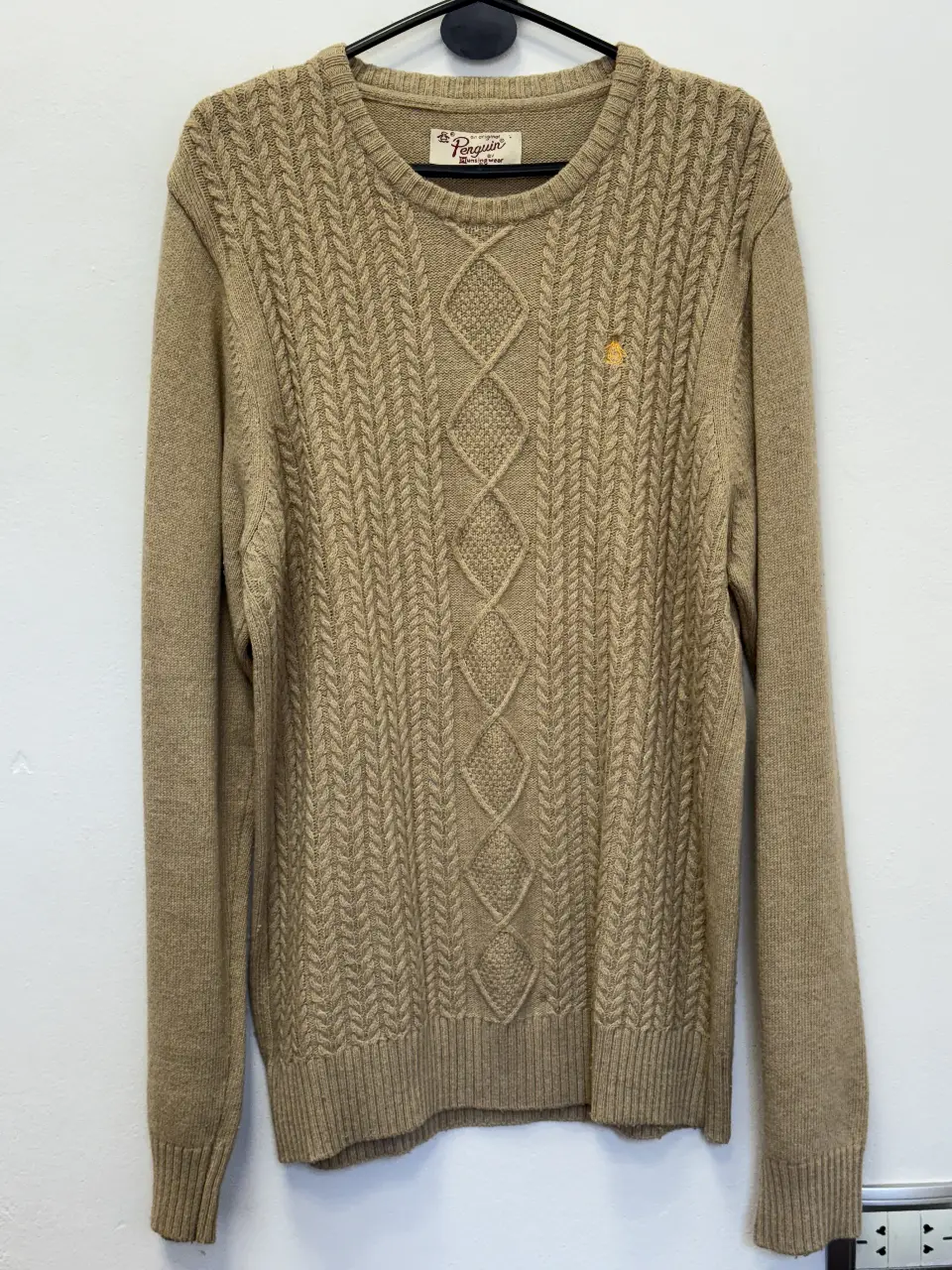 Sweater de hombre Penguin, color crudo, con diseño de trenzas y rombos en el frente. Cuello redondo y detalle del logo de la marca en amarillo. Ideal para un look casual y abrigado.