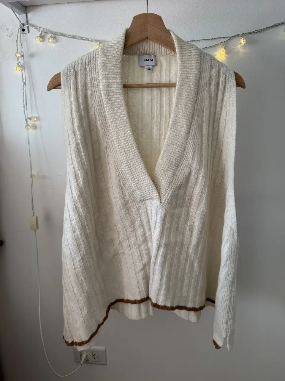 Chaleco tejido de lana color blanco con detalles marrones en el borde inferior. Cuello en V y corte recto. Ideal para un look casual y abrigado.