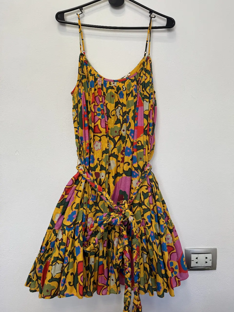 Vestido mini de verano con estampado floral en tonos amarillos, rosas, azules y verdes. Diseño con tirantes finos, cintura con cinturón y falda con vuelo plato. Ideal para un look fresco y bohemio.