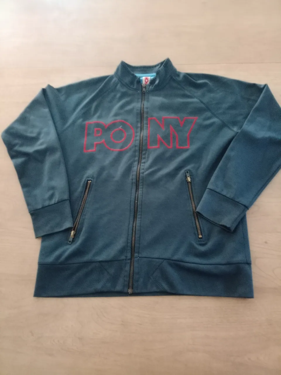 Buzo deportivo vintage de la marca Pony, con cierre completo y logo grande en el frente. Tiene dos bolsillos de cierre. Ideal para un look casual y retro.