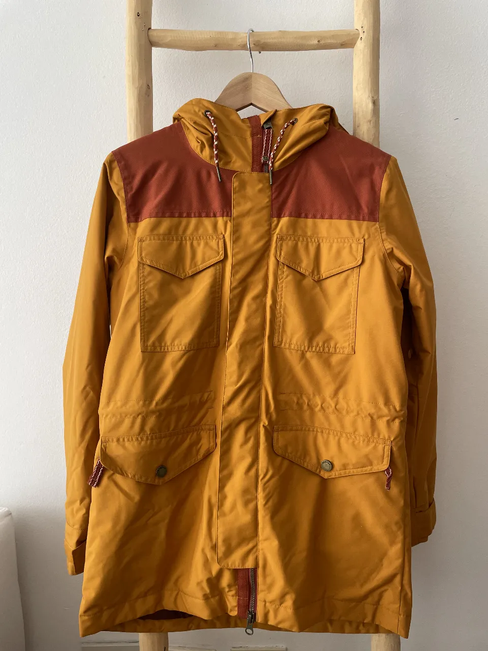 Campera Burton amarilla con detalles en marrón, ideal para actividades esquiar/actividades al aire libre. Posee capucha, múltiples bolsillos y un diseño funcional y moderno.