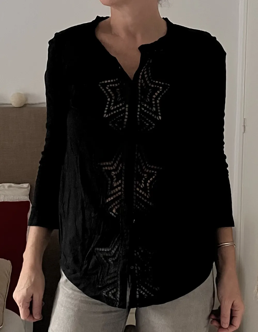 Blusa negra con mangas 3/4 y detalles bordados en forma de estrellas en el frente. Posee cuello redondo con pequeños volados y botones en la parte superior.