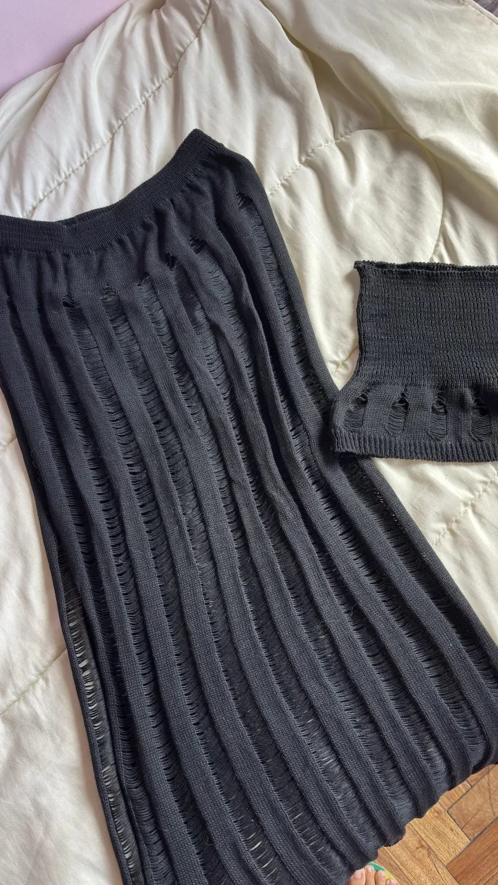 Conjunto de dos piezas de tejido negro con roturas y aberturas. Incluye un top corto y una falda larga.