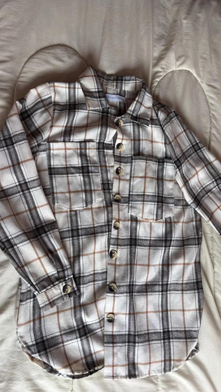 Camisa a cuadros de manga larga con botones al frente y en los puños. Posee dos bolsillos en el frente.