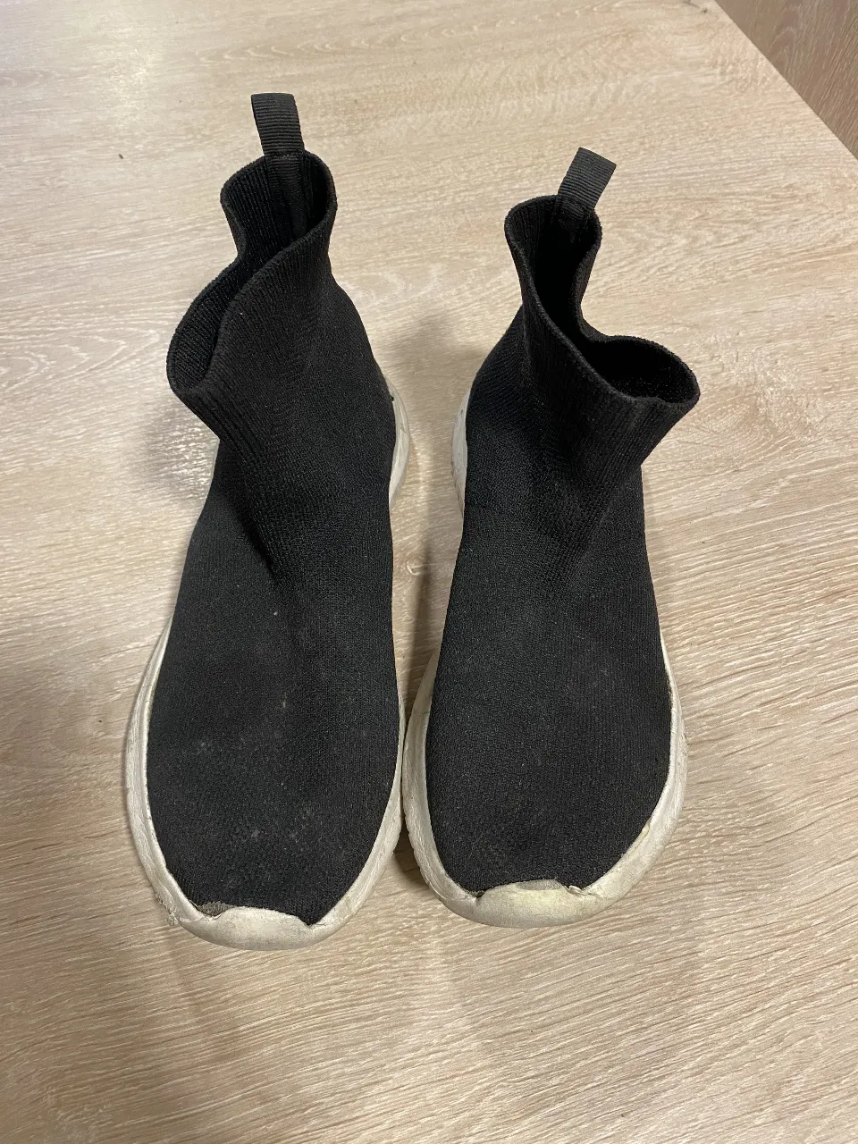 Zapatillas tipo botín de color negro con suela blanca. Diseño moderno y cómodo, ideales para un look casual y urbano.
