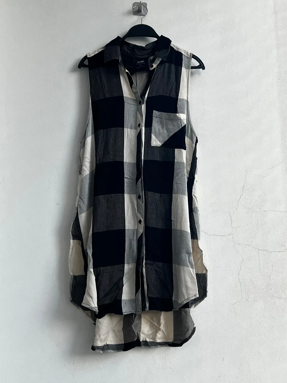 Camisa sin mangas a cuadros en blanco y negro, ideal para un look casual y moderno. Con un bolsillo en el pecho y botones frontales, perfecta para combinar con jeans o shorts.