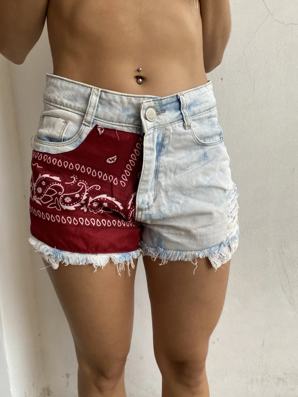 Short de jean de mujer con diseño único. Un lado en denim celeste claro con detalles deshilachados y el otro lado con tela de bandana roja estampada. Un estilo moderno y audaz para un look casual y con onda.