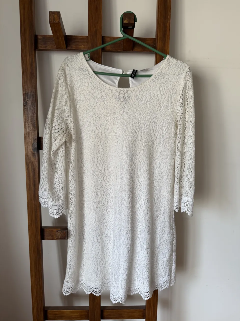Vestido blanco de encaje con mangas 3/4 y detalles de puntilla en puños y ruedo. Posee un recorte en forma de lágrima en la espalda con un botón para cerrar. Ideal para un look romántico y delicado.