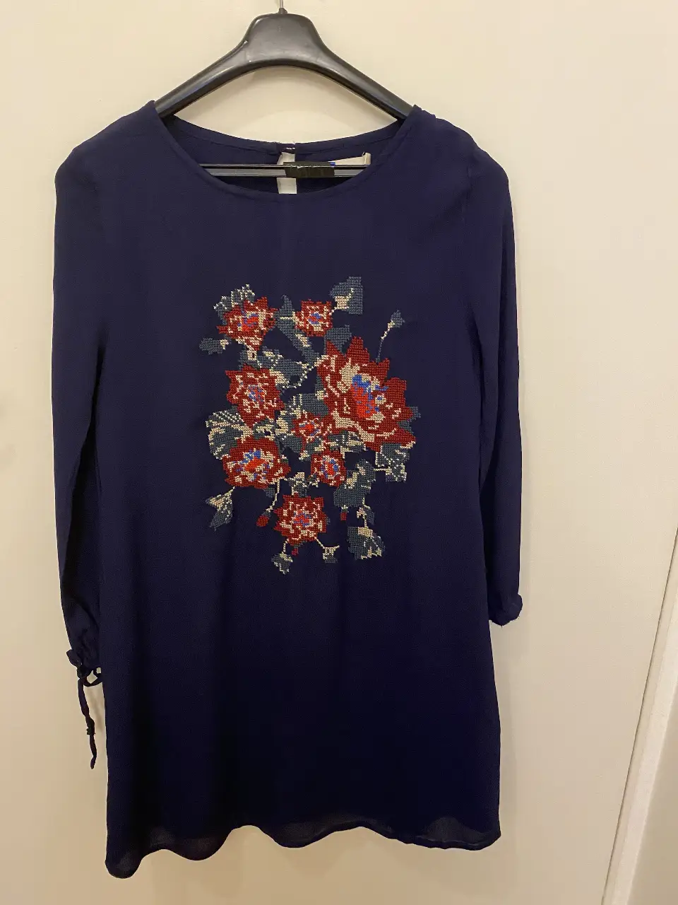 Vestido midi azul marino con bordado floral en el frente. Manga larga con detalle de lazo en los puños. Talle 1 de la marca Uma.