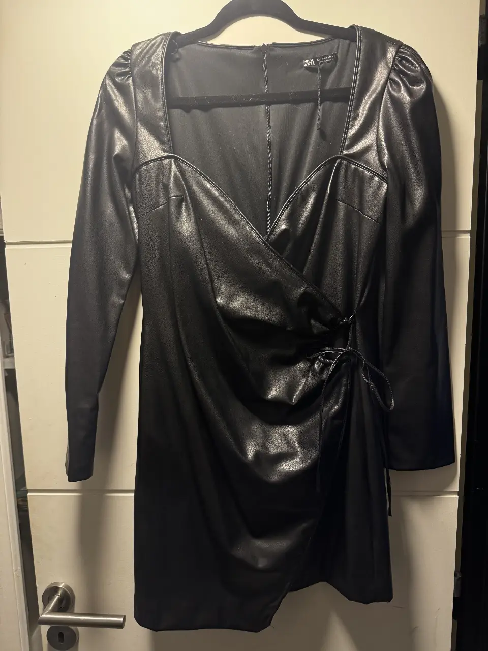Vestido mini de cuero sintético negro, con escote cuadrado y detalle de lazo en la cintura. Ideal para una salida nocturna o evento especial. Sin uso. 