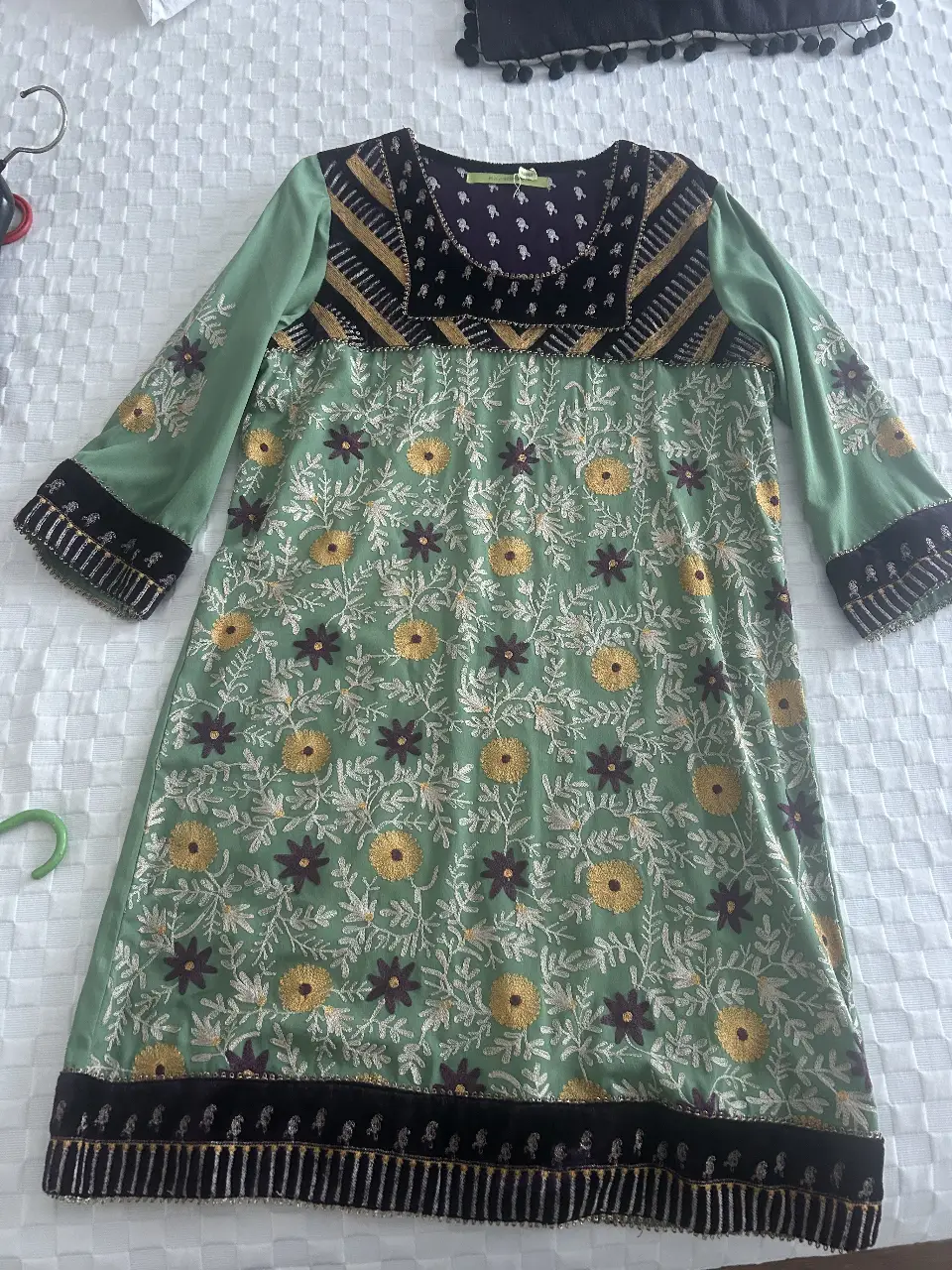Vestido midi de mujer con bordados florales en tonos amarillos y detalles en negro. Diseño artesanal con mangas largas y cuello redondo. Ideal para un look casual con un toque bohemio.