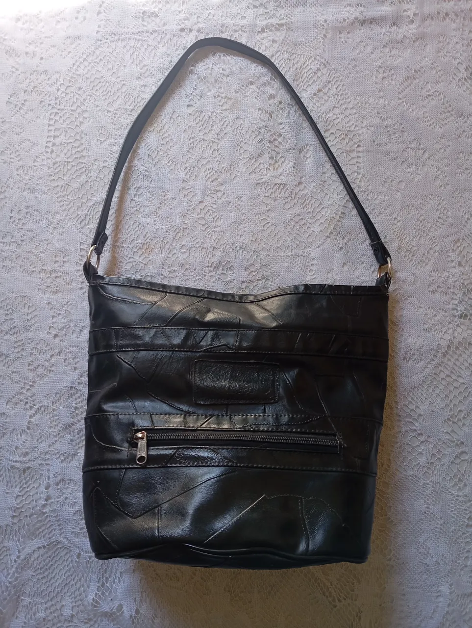 Cartera negra con correa de hombro. Posee un bolsillo en el interior y un bolsillo exterior con cierre.