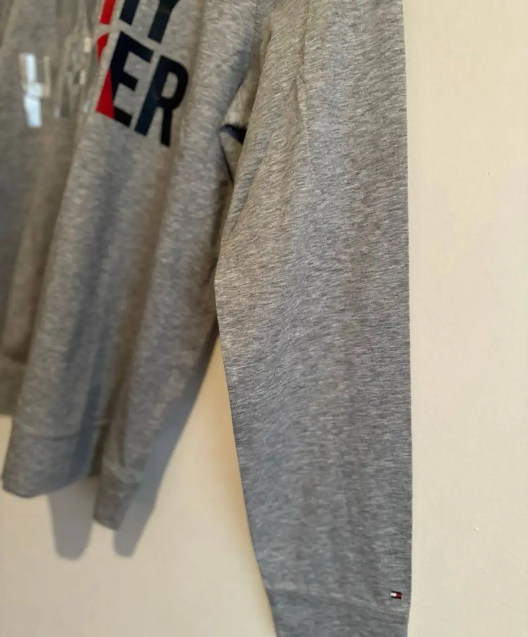 Buzo canguro gris de hombre con capucha y estampado Tommy Hilfiger en el frente. Ideal para un look casual y cómodo.