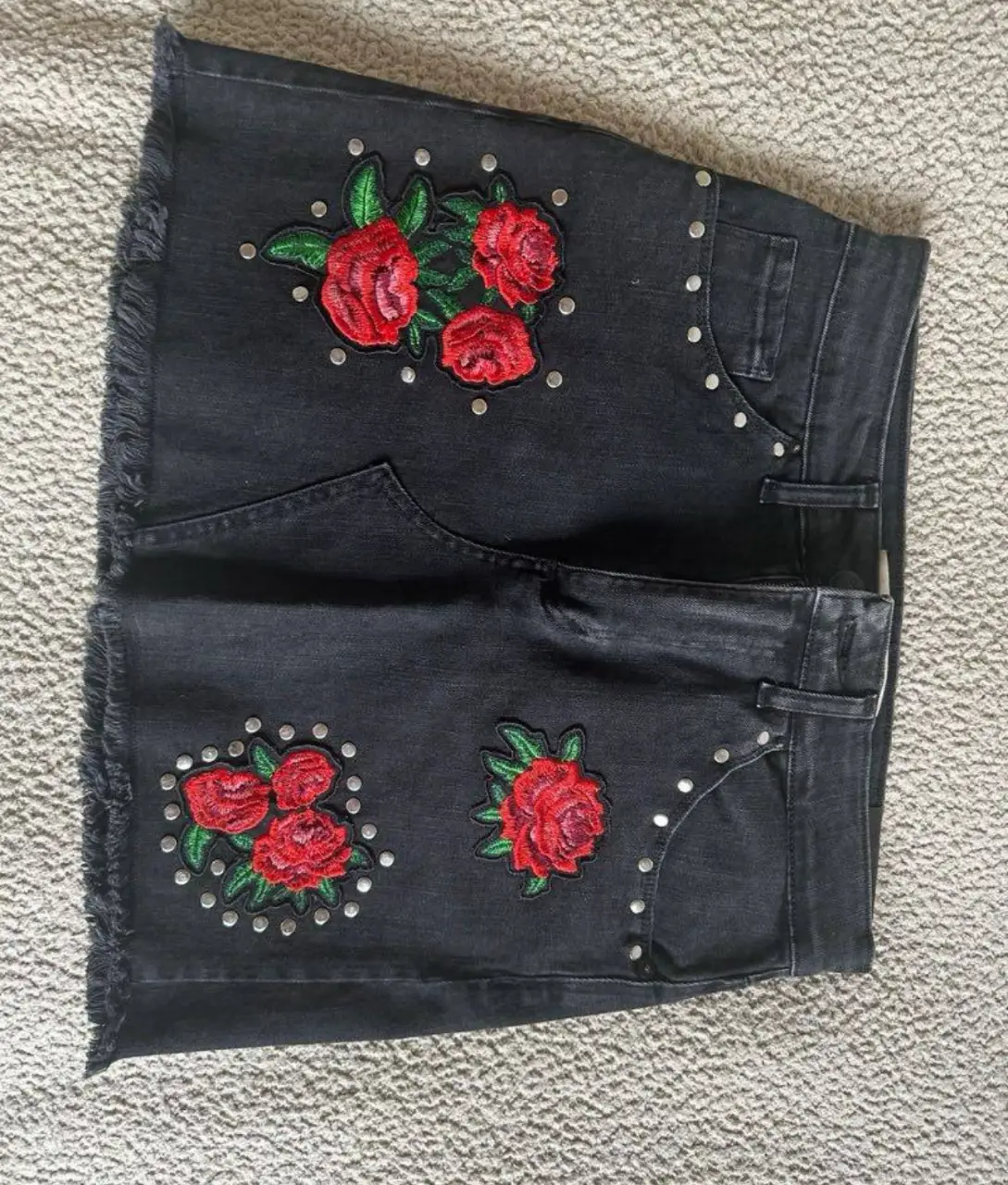 Pollera de jean negra con detalles de flores rojas bordadas y tachas. Ideal para un look casual y canchero.