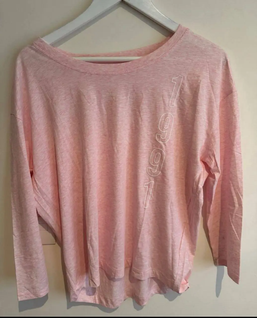 Remera manga larga rosa con estampado "1991" en la parte delantera y "ARMANI EXCHANGE" en la espalda. Ideal para un look casual y moderno.