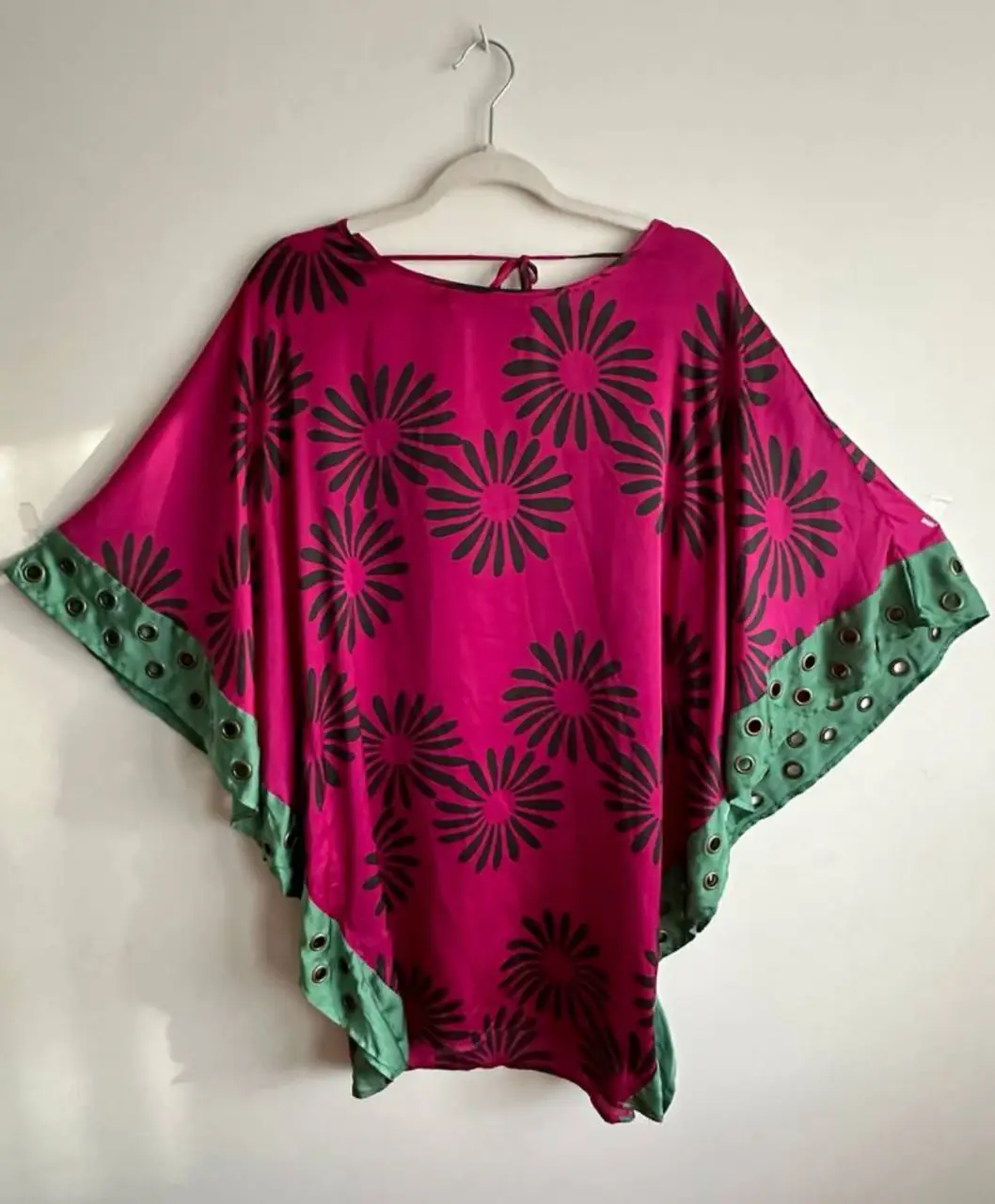 Vestido midi de seda con estampado floral en tonos fucsia y detalles en verde. Diseño holgado con mangas amplias y terminaciones con ojales. Ideal para un look bohemio y elegante.