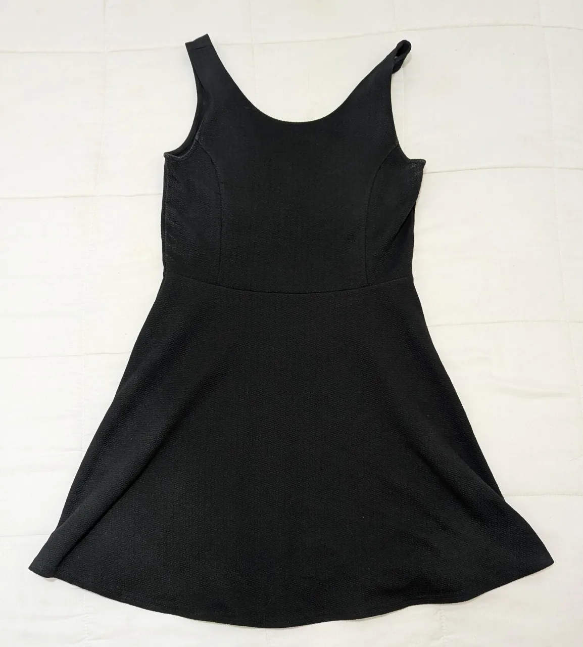 Vestido negro sin mangas, con escote redondo y falda con movimiento.