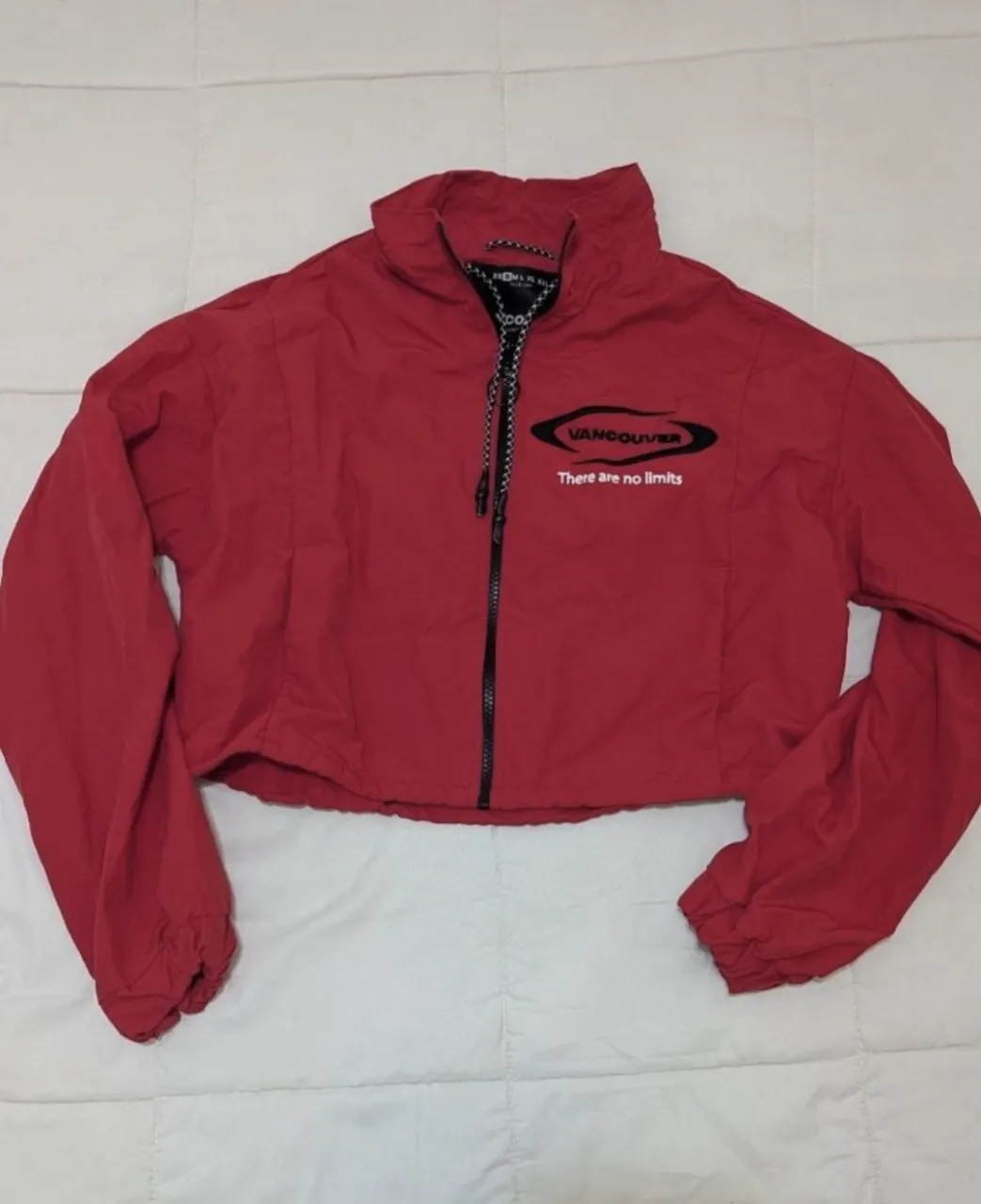 Campera corta roja con cierre central y logo de Vancouver bordado en negro. Posee cordones en el cuello y puños con elástico.