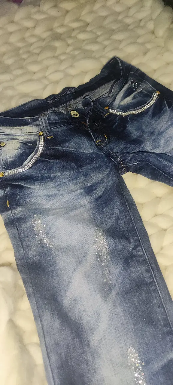 Jean de mujer azul con detalles de brillos en bolsillos y frente. Tiro medio, ideal para un look casual con un toque de brillo.