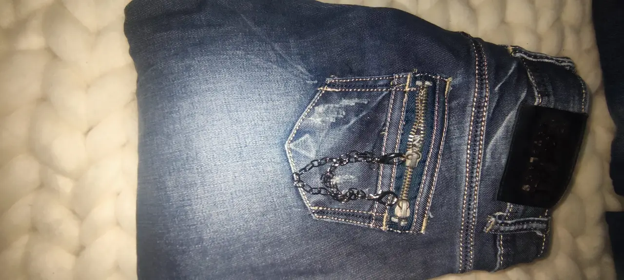 Jeans rectos de mujer, azul gastado con detalles de roturas y cierre con cadena en bolsillo trasero. Un clásico para cualquier ocasión.