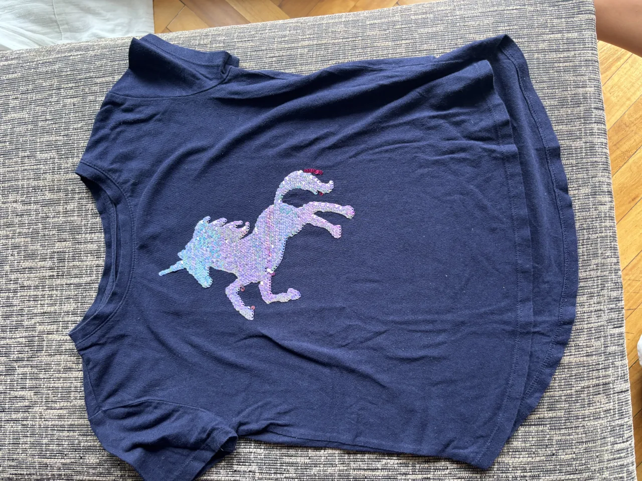 Remera azul marino con un aplique de unicornio lleno de lentejuelas iridiscentes. ¡Perfecta para las pequeñas soñadoras!