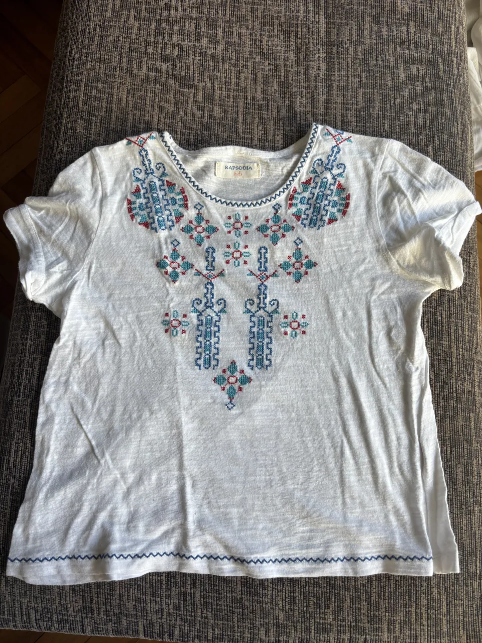 Remera blanca de manga corta con un hermoso bordado de estilo étnico en el cuello y el frente. El bordado combina tonos de azul y rojo, dándole un toque vibrante y artesanal. Perfecta para un look casual y con onda.