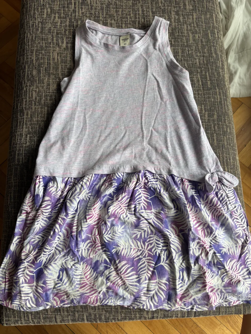 Vestido de verano con estampa de hojas en tonos violetas y blancos. La parte superior es lisa en gris melange con detalles en rosa. Ideal para días cálidos y salidas informales.